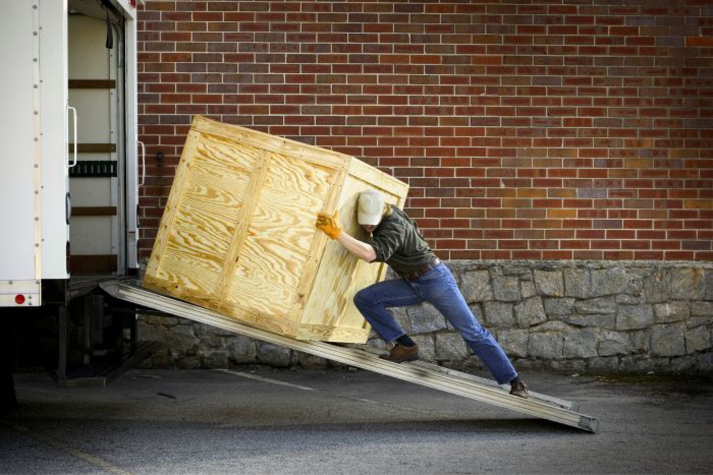 Man pushing large wooden box up ramp into box truck